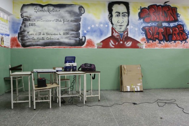 A voting machine is seen in front of a mural depicting South American independence leader Simon Bolivar at a school in Caracas, December 4, 2015. Venezuela will hold parliamentary elections on December 6. REUTERS/Marco Bello. FOR EDITORIAL USE ONLY. NO RESALES. NO ARCHIVE.