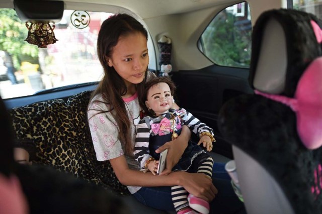 TO GO WITH 'Thailand-lifestyle-society-religion' by Jerome TAYLOR This picture taken on January 28, 2016 shows a student and helper holding a "luuk thep" (child angel) doll in a car on the way to a Buddhist temple outside the house of doll collector, producer and trader, Mananya Boonmee (not pictured) in Nonthaburi on the outskirts of Bangkok.  Seats at restaurant tables, in-flight meals, religious ceremonies and designer clothes are just some of the items Thais can buy their lucky "angel dolls", the latest celebrity-fuelled supertitious craze that has swept the country much to the dismay of the kingdom's conservative military rulers.  AFP PHOTO / Christophe ARCHAMBAULT / AFP / CHRISTOPHE ARCHAMBAULT