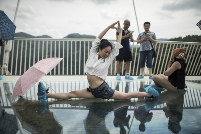 A woman poses on the world's highest and longest glass-bottomed bridge is seen above a valley in Zhangjiajie in China's Hunan Province on August 20, 2016. / AFP PHOTO / FRED DUFOUR