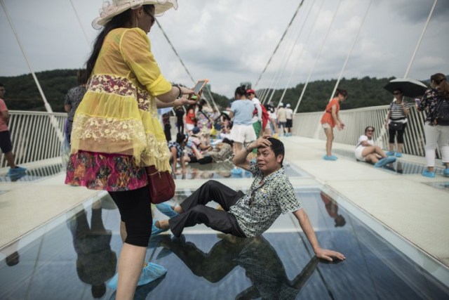 A tourist takes a photograph on the world's highest and longest glass-bottomed bridge above a valley in Zhangjiajie in China's Hunan Province on August 20, 2016. / AFP PHOTO / FRED DUFOUR