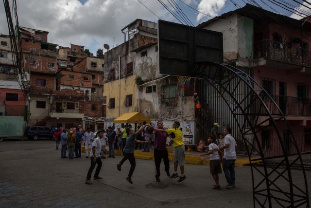 CAR01. CARACAS (VENEZUELA), 10/09/2016.- Un grupo de personas juegan baloncesto mientras esperan por un plato de sancocho hoy, sábado 10 de septiembre del 2016, en la ciudad de Caracas (Venezuela). En el barrio la Unión, ubicado en la favela más grande de América Latina asentada en el este de Caracas, se preparó hoy un gran "sancocho" como se le conoce en Venezuela a la sopa cocinada con varios tipos de verduras y carnes, para alimentar a los vecinos, muchos de ellos con varios días de hambre. EFE/MIGUEL GUTIÉRREZ