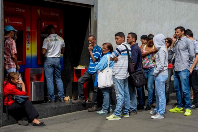 People queue to withdraw money from an automated teller machine (ATM) in Caracas on December 1, 2016. Venezuelan banks guaranteed their continued operation, after rumors about a close in December to adjust to an alleged issuance of bills of higher denomination. At the moment, the note of highest denomination is the one of 100 bolivars, that is just enough to buy a sweet. / AFP PHOTO / Federico PARRA