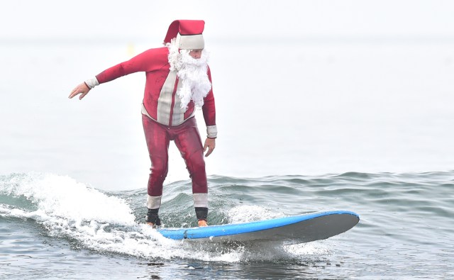 Surfing Santa, Michael Pless, surfs at Seal Beach, California on December 10, 2016, where he runs a surfing school and has every December since in 1990's gone out to surf in his Santa Claus outfit. / AFP PHOTO / Frederic J. BROWN