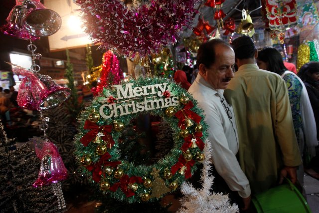 People walk past an artificial decoration wreath hanging outside a shop selling various items for Christmas celebrations in Karachi, Pakistan, December 24, 2016. REUTERS/Akhtar Soomro