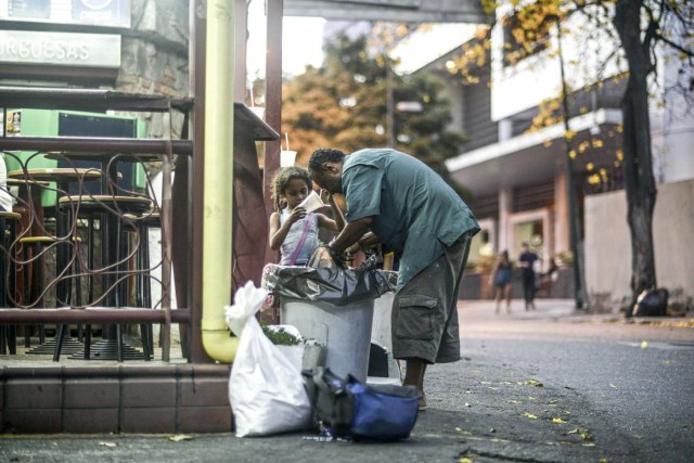 A man and a girl scavenge for food in the streets of Caracas on February 21, 2017. Venezuelan President Nicolas Maduro is resisting opposition efforts to hold a vote on removing him from office. The opposition blames him for an economic crisis that has caused food shortages. / AFP PHOTO / JUAN BARRETO / TO GO WITH AFP STORY BY Alexander Martinez