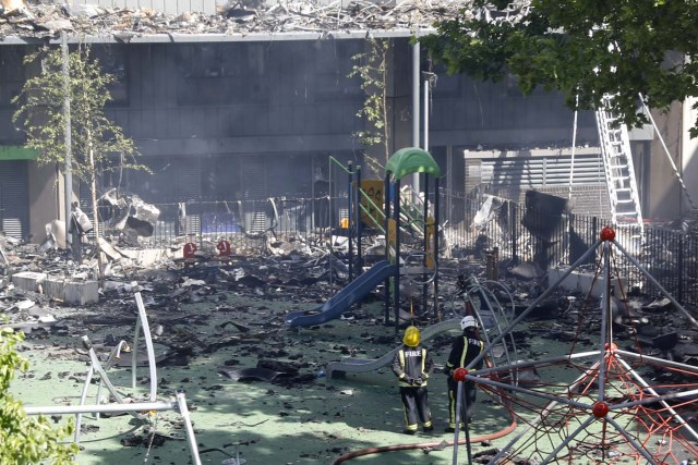 Firemen standing among debris in a childrens playground look at Grenfell Tower, a residential tower block in west London that was gutted in a huge blaze on June 15, 2017. Firefighters searched for bodies today in a London tower block gutted by a blaze that has already left 17 dead, as questions grew over whether a recent refurbishment contributed to the fire. / AFP PHOTO / Tolga AKMEN