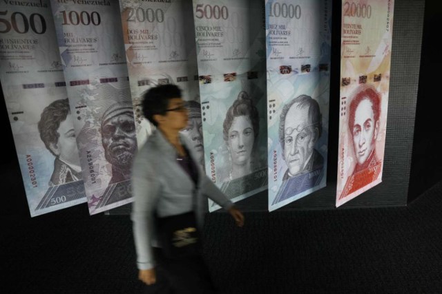 Una persona camina delante de unas pancartas con imágenes de los billetes de Venezuela en la sede del Banco Central en Caracas, 23 de mayo de 2017. REUTERS/Carlos Barria