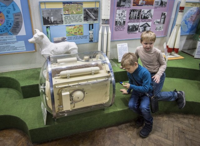 Una foto tomada el 1 de noviembre de 2017 muestra a niños jugando un juego en un teléfono móvil junto al perro Contenedor espacial Laika usado para entrenamientos antes de despegar para orbitar la Tierra el 3 de noviembre de 1957, en la Casa Central de Aviación y Cosmonáutica en Moscú. Tres años y medio antes de que el cosmonauta ruso Yuri Gagarin se convirtiera en el primer hombre en el espacio, un perro llamado Laika fue en 1957 el primer ser vivo en orbitar la Tierra. El extraviado de Moscú es uno de los muchos animales que precedieron a los humanos en la conquista del espacio; como la mayoría de los otros, ella no sobrevivió. / AFP PHOTO / Mladen ANTONOV