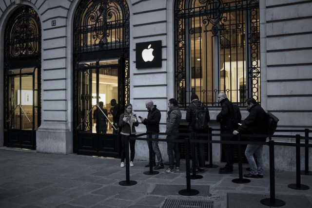 An Apple employee (L) chats with customers queuing to get their pre-ordered iPhones outside an Apple shop early morning on the release day of the new iPhone X in Paris on November 3, 2017. / AFP PHOTO / PHILIPPE LOPEZ