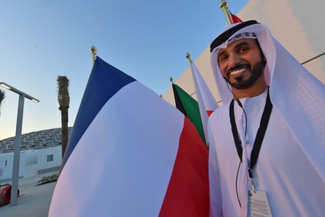 An Emirari man stand next to a French flag at the entrance of the Louvre Abu Dhabi Museum on November 8, 2017 prior to the inauguration of the museum on Saadiyat island in the Emirati capital. More than a decade in the making, the Louvre Abu Dhabi is opening its doors bringing the famed name to the Arab world for the first time. / AFP PHOTO / ludovic MARIN