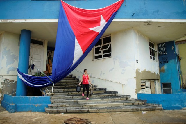 Una mujer limpia la entrada de un edificio junto a una bandera cubana que se colgó a secar después de que el huracán Irma causó inundaciones y un apagón, en La Habana, Cuba, el 11 de septiembre de 2017. REUTERS / Alexandre Meneghini