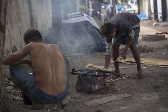 Venezuelan refugees cook inside a shelter in the city of Boa Vista, Roraima, Brazil, on February 24, 2018. According with local authorities, around one thousand refugees are crossing the Brazilian border each day from Venezuela. With the constant influx of Venezuelan immigrants most are living in shelters and the streets of Boa Vista and Paracaima cities, looking for work, medical care and food. Most are legalizing their status to stay and live in Brazil. / AFP PHOTO / MAURO PIMENTEL