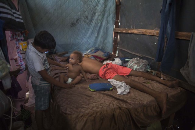 A boy plays with his little brother as their father sleeps, inside a tent at a shelter for Venezuelan refugees in the city of Boa Vista, Roraima, Brazil, on February 24, 2018. When the Venezuelan migratory flow exploded in 2017 the city of Boa Vista, the capital of Roraima, 200 kilometres from the Venezuelan border, began to organise shelters as people started to settle in squares, parks and corners of this city of 330,000 inhabitants of which 10 percent is now Venezuelan. / AFP PHOTO / MAURO PIMENTEL