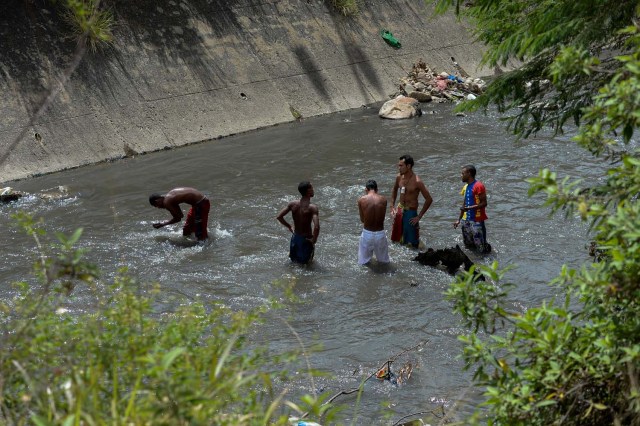 Los hombres buscan metales valiosos en un canal de aguas residuales en el río Guaire, en Caracas, el 1 de febrero de 2018. Decenas de jóvenes buscan diariamente joyas perdidas en el río Guaire, donde drenan las alcantarillas de Caracas. Encontrar oro es su ilusión, pero una pieza de alambre de cobre es suficiente para paliar el hambre. / AFP PHOTO / FEDERICO PARRA