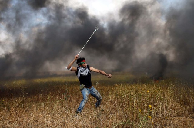 A Palestinian hurls stones at Israeli troops during clashes, during a tent city protest along the Israel border with Gaza, demanding the right to return to their homeland, the southern Gaza Strip March 30, 2018. REUTERS/Ibraheem Abu Mustafa