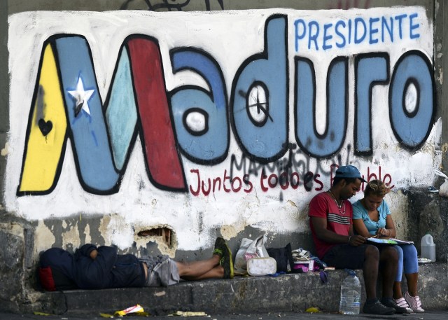 Personas junto a un graffiti alusivo a la publicidad electoral del presidente venezolano y candidato a la reelección, Nicolás Maduro Caracas, el 11 de mayo de 2018. Los ciudadanos venezolanos se enfrentarán a las elecciones presidenciales del 20 de mayo en medio de una crisis socioeconómica severa, con hiperinflación estimada en 13.800% por el FMI para 2018, y la escasez de alimentos, medicinas y otros productos básicos. / AFP PHOTO / Luis ROBAYO