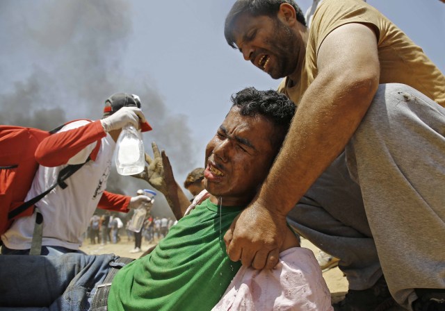 Un palestino asiste a un manifestante herido durante enfrentamientos con las fuerzas de seguridad israelíes cerca de la frontera entre Israel y la Franja de Gaza, al este de Jabalia el 14 de mayo de 2018, mientras los palestinos protestan por la inauguración de la embajada de Estados Unidos tras su controvertido traslado a Jerusalén. / AFP PHOTO / MOHAMMED ABED