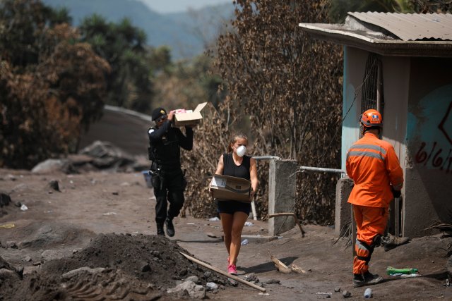 Un policía ayuda a un residente a llevar las pertenencias recuperadas de su casa en un área afectada por la erupción del volcán Fuego en San Miguel Los Lotes en Escuintla, Guatemala, el 11 de junio de 2018. REUTERS / Jose Cabezas